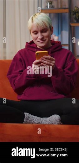 Woman with short blonde hair sitting on sofa uses mobile phone smiles at night home apartment. Girl texting share messages content on smartphone social media applications online, watching relax movie Stock Video Footage - Alamy