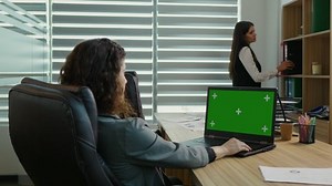 Woman side view working on laptop with chroma key screen. Female browsing internet on a green screen laptop in the office.