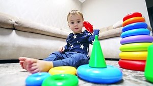 Smart toddler plays with a pyramid sitting on the floor. Calm little baby having playtime at home. Low angle view.