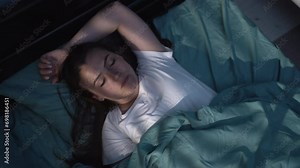 Young woman sleeping on a bed in bedroom or hotel room at night, top view. Blue nightly light shining through the window Stock 비디오