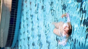 Beautiful woman in white swims on her back in the pool