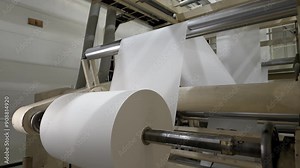 Paper sheet coiled by metal rollers of production line in plant workshop. Machine tools works at papermaking factory. Manufacture technology