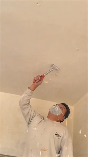 scraping off old white ceiling paint manually using a small metal scraper tool in renovation area