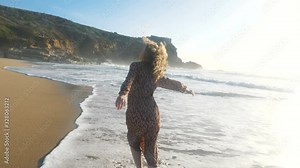 woman in dress runs along wet beach washed by peaceful ocean