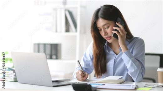 Businesswoman working on paperwork and talking to someone on mobile phone while reading and analyzing monthly work schedule.