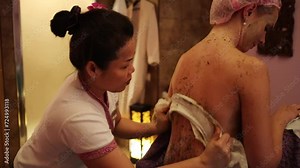 Hands of therapist remove scrub from skin of female back in spa salon