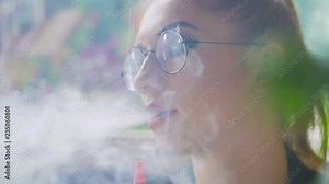 A young girl sitting in a cafe smoking a hookah, slowly exhaling thick white smoke.