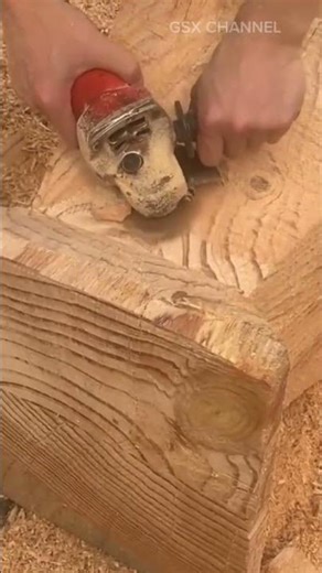 Smoothing the surface of a thick brown wooden block using an electric angle grinder in a workshop