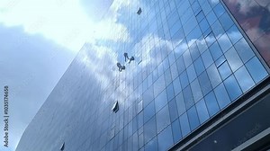 Window Cleaners Working on Glass High-Rise Building, Window cleaners suspended on a skyscraper, methodically cleaning the reflective glass facade of a modern high-rise building.