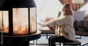 Woman warming her hands at fireplace. Young female is relaxing in house during winter. She is wearing sweater and gloves.