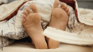 A mother tickling the feet of her child still in bed in the morning. Straight shot.