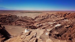 Aerial view of model wearing white dress standing in the cliff of a rocky desert, 4k