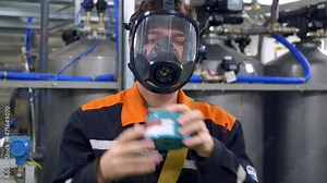 The worker puts on a mask and winds a gas mask filter on it. Preparation for work in conditions of infection or poisonous substances. Work in hazardous production and industry.