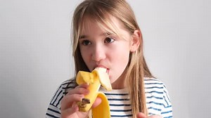 Blonde Girl Eating Banana in Front of Backdrop