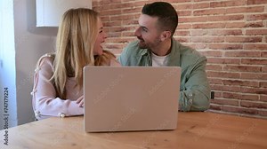 Happy man and woman using computer together while sitting in the living room. Young smiling couple connected on internet with device at their home