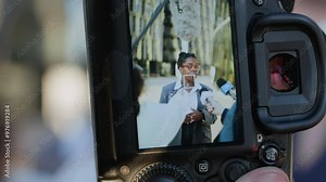 Through digital camera shot of confident African American businesswoman being interviewed by several TV reporters outdoors
