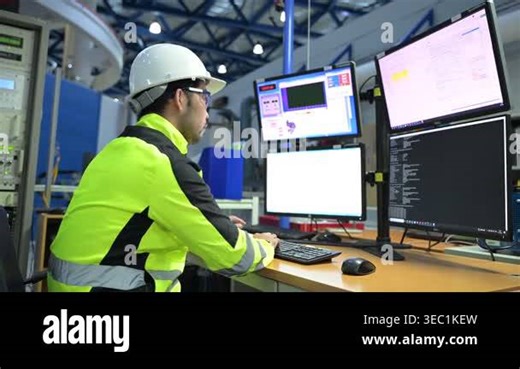 Man wearing hard hat and safety jacket working at multiple computer screens in an industrial setting Stock Video Footage - Alamy