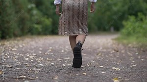 Live camera follows steps of slim young elegant woman strolling outdoors on park alley. Back view of unrecognizable Asian confident lady in skirt and boots walking outdoors enjoying leisure