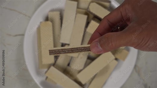 Hand picking up a wafer biscuit from a pile on a textured surface