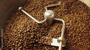 Production of freshly roasted coffee beans. Industrial mixing machine mixes roasted coffee beans in roaster, close up. Roasting process in factory. Food and drink background for cafe. Slow motion.