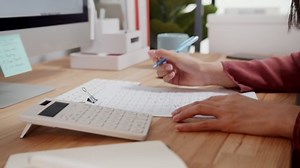 Close up of Businesswoman or female accountant freelancer hand using a calculator calculating expenses, tax, analysis financial data, and taking notes on notebook working from home. Financial Concept.