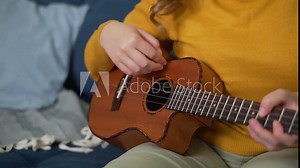 Performance of song on ukulele. One hand gently beats the guitar strings to the rhythm, the fingers of the other hand clamp musical chords on the neck of the instrument. Music school, online training