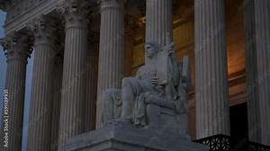 Authority of Justice sculpture in front of US Supreme Court building with light behind at night in Washington DC.