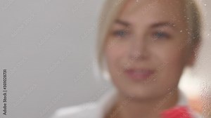 Close-up reflection of lovely cleaning lady appearing on mirror surface during hotel clean up. Female hand wiping mirror after spraying detergent, charming maid smiling while looking at own reflection
