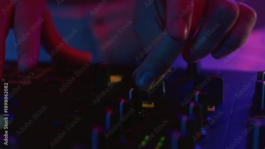 Man DJ playing music on electronic mixer controller at disco club. Male disk jockey mixing sound on set in night club. Hand of guy on turntable panel. Close up. Clubbing vibe, neon party, mix console