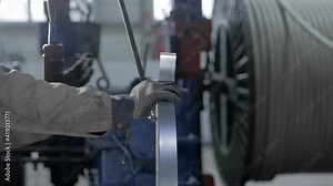 A close-up of the worker's hand is pressed by the electric lift button to move the bobbin with metal tape