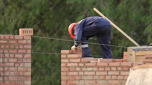 The bricklayer building a brick wall, the mason wears helmet and overalls