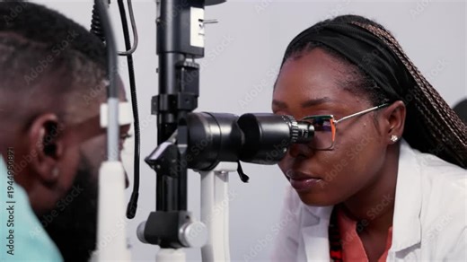 African female optometrist performing an eye exam on a male patient with a slit lamp machine