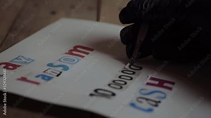 Kidnapper in black gloves making a ransom note for cash