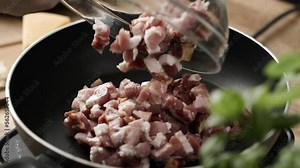 Carbonara recipe; Adding chopped bacon into hot pan and spreading out evenly with wooden spatula; rendering bacon, steam visible; close up, 4k, slow motion