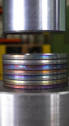 Nic Davis on Instagram: "Watch as heat-treated bearing plates with mesmerizing violet, gold, and blue surfaces get crushed under extreme pressure. The stack binds and shears, releasing dark violet-grey grease while metal fragments scatter everywhere in this insane hydraulic press moment!"