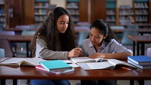 Two young women studying together in a library, surrounded by books | Premium Stock Video Footage