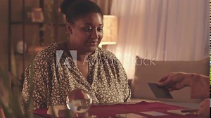 Waist up slowmo of young plus size African American woman watching fortune teller laying out tarot cards during seance