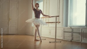 Professional ballet dancer lady in tutu exercising at barre, slow motion. Beauty and grace of ballerina, hobby and dream, workout in dancehall, slender female figure in rehearsal room, art concept