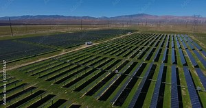aerial over solar panel field, with mountains and wind turbines in background. drone flight aerial over solar panel field, mountains and wind turbines in the distance, springtime southern California.