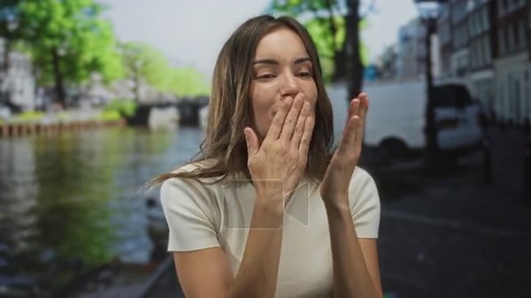Woman blows kiss with hand over lips, smiling in white top on street by canal in amsterdam; playful affection Stock Video Footage - Alamy