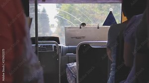 Inside view of a regular bus. The landscape changes behind the windshield. People are sitting in the passenger seats. Passage between the seats. Summer sunny day. Public transport