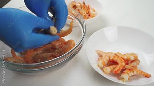 Cleaning shrimp. Close-up of blue gloved hands removing the head and shell of a shrimp after cooking.