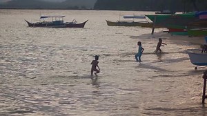 Silhouettes of happy Filipino children playing on the beach at sunset.