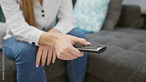 A young blonde woman in a white shirt holding a remote control in a modern living room.