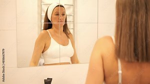 Woman gazes at her reflection in bathroom mirror. Mirror captures serene moment of self-reflection. Intimate scene highlights beauty and tranquility. Perfect for themes of self-care and mirror imagery