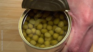 Hands opening tin can with green peas kernels ready to eat meal close-up. Showing how to open a can with pull tab. Non perishable food storage products in the home kitchen