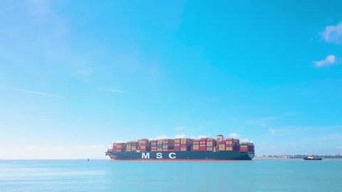 01 MARCH 2025 An MSC shipping container fully laden being lead out to sea by a tugboat at the port of Felixstowe, East Suffolk, UK on a sunny spring day, blue sky, space for text
