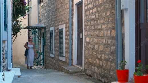 Woman walking down an old european street. Pretty woman in a summer dress walking down a narrow stone street in a charming old european town during her vacation, smiling and enjoying the atmosphere