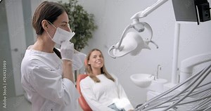 A female dentist puts on a medical mask and gloves and opens new instruments to examine teeth. A female dentist examines and treats a patient's teeth in a dental office.