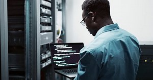 Laptop, data engineer and black man coding on software for cybersecurity in business with server room. Professional, employee and African male person programming on database with technology online